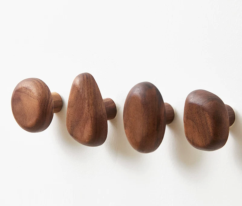 Set de 4 patères galet en noyer massif, formes variées, fixées au mur sur fond clair