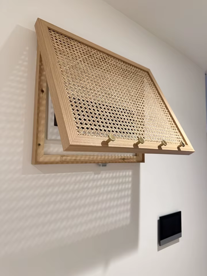 Cache-compteur électrique cannage et bois massif zoom sur le Cache-compteur électrique design en bois massif clair et façade en cannage rotin, équipé de 4 crochets dorés.