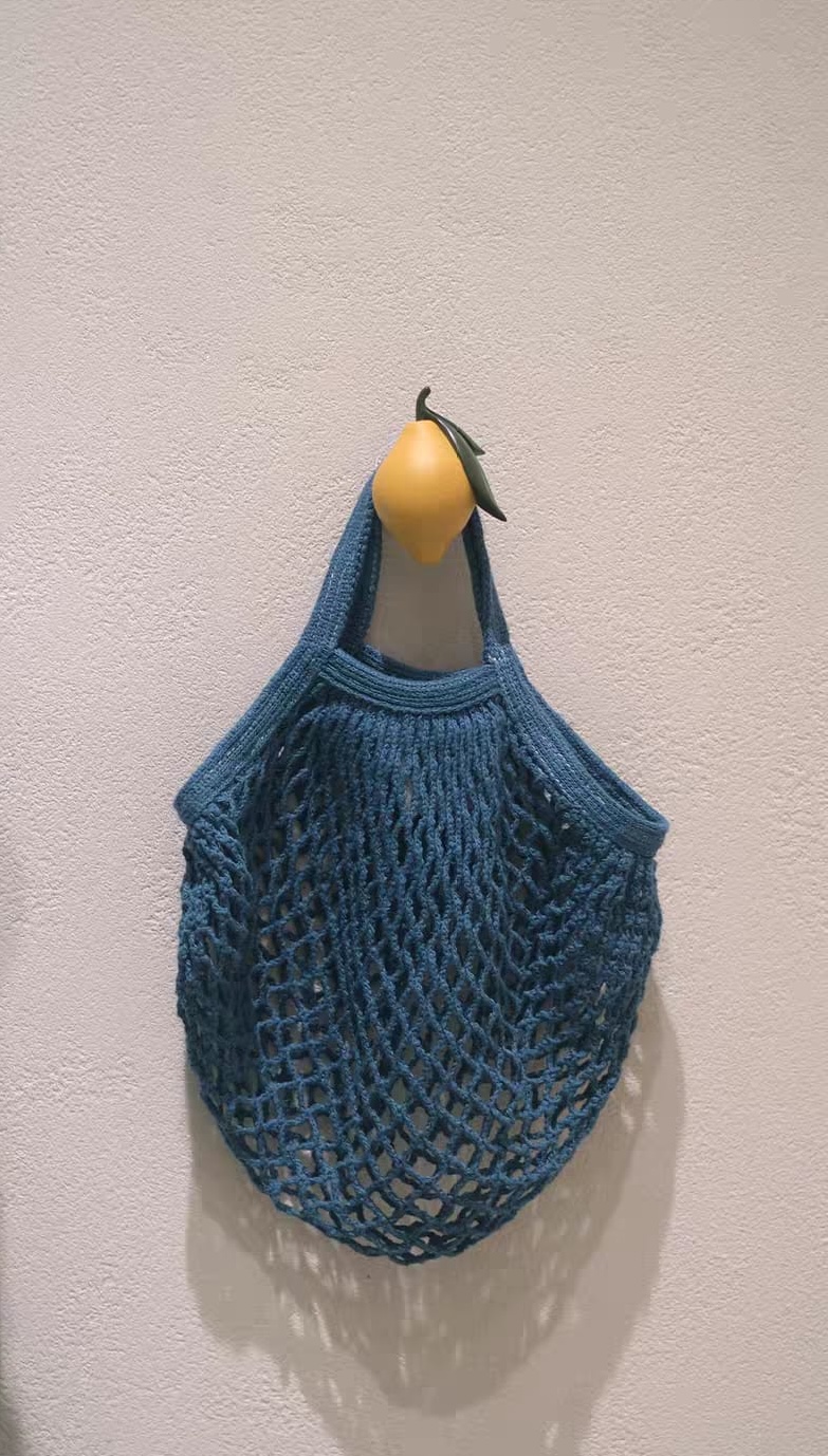Patère murale fruit — pomme, fraise, citron en résine Une patère en forme de citron soutient un sac bleu