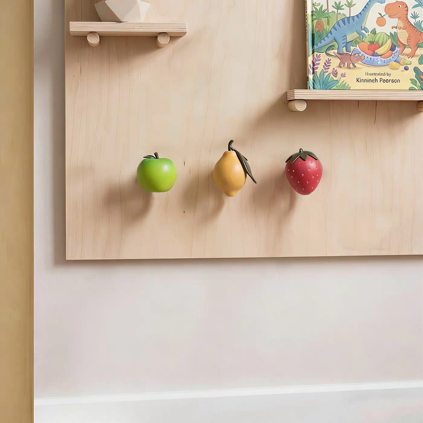 Patère murale fruit — pomme, fraise, citron en résine Des patères en forme de pomme, citron et fraise fixés sur un mur en bois.