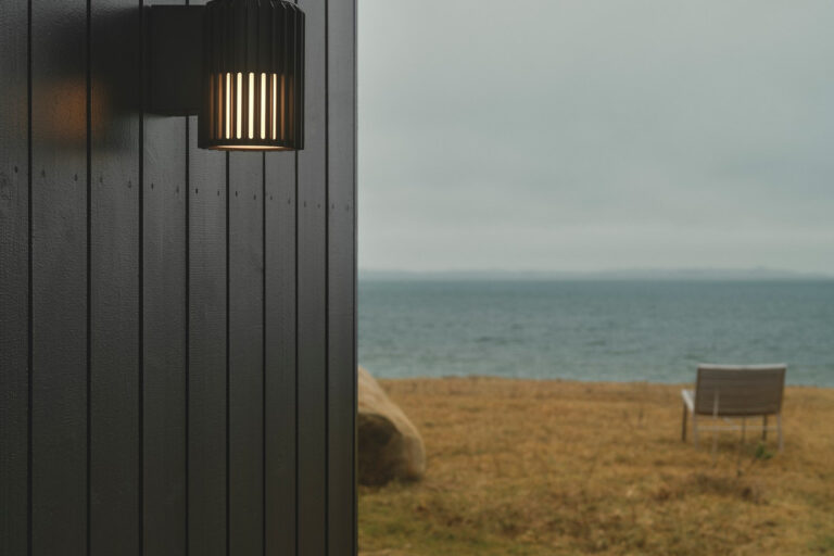 Applique extérieure murale Aludra Nordlux installée sur une façade en bois face à la mer