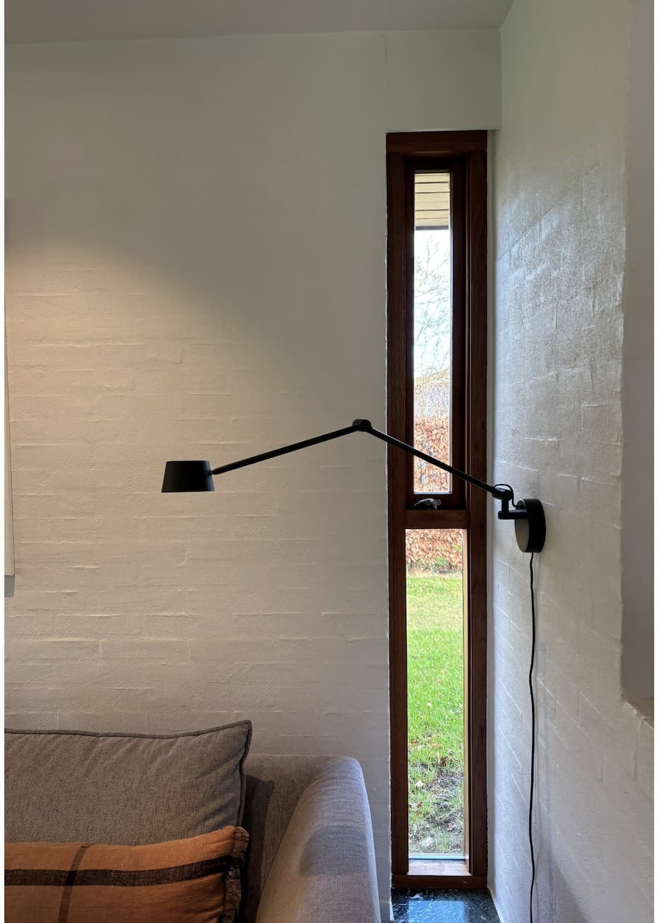 applique articulée Direction Wall Antidark noire fixée au mur d'un salon près d'un canapé