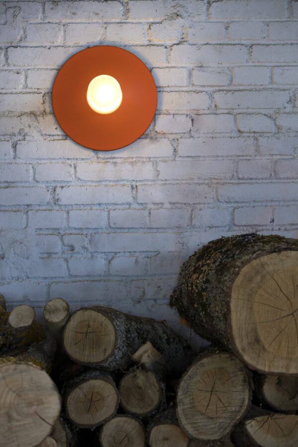 applique Cooper Roger Pradier orangé pur allumée sur un mur de brique blanchi