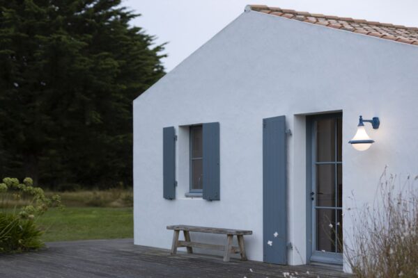 applique extérieure Dallas version descendante teinte bleu acier sur une maison blanche à volets bleus