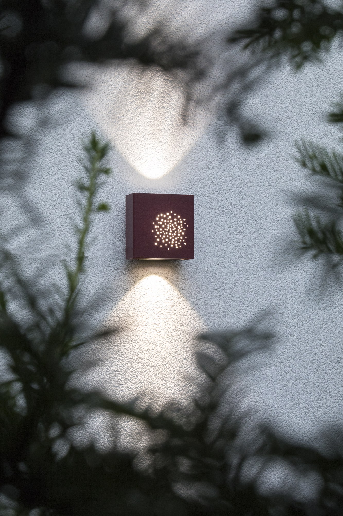 Applique extérieure Klint LED up and down par Roger Pradier applique extérieure Klint face perforée rouge vin, motif de trous lumineux sur un mur clair