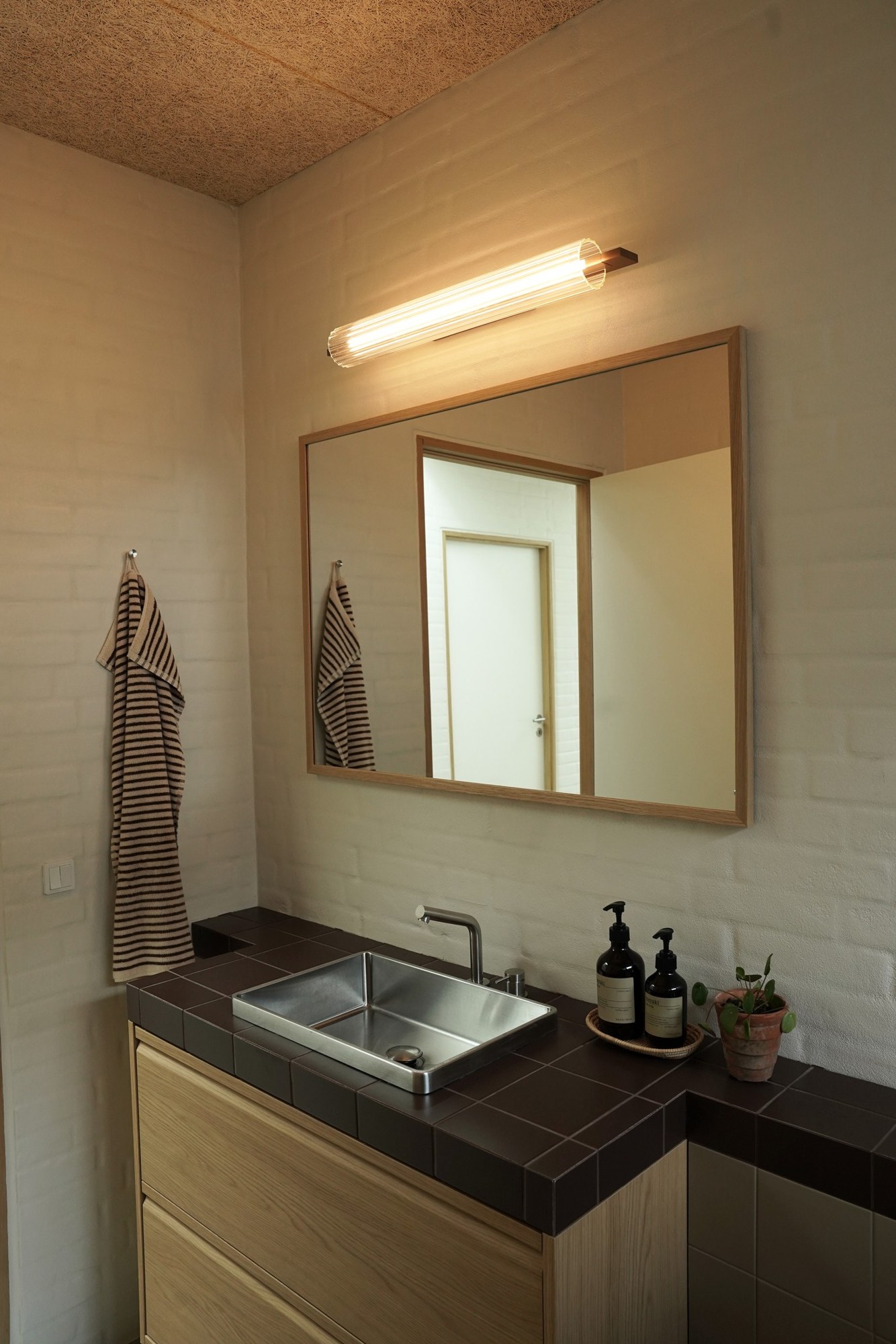 Applique Lirra LED en verre côtelé par Antidark Applique Lirra LED 70 cm posée à l'horizontale au-dessus d'un miroir de salle de bain