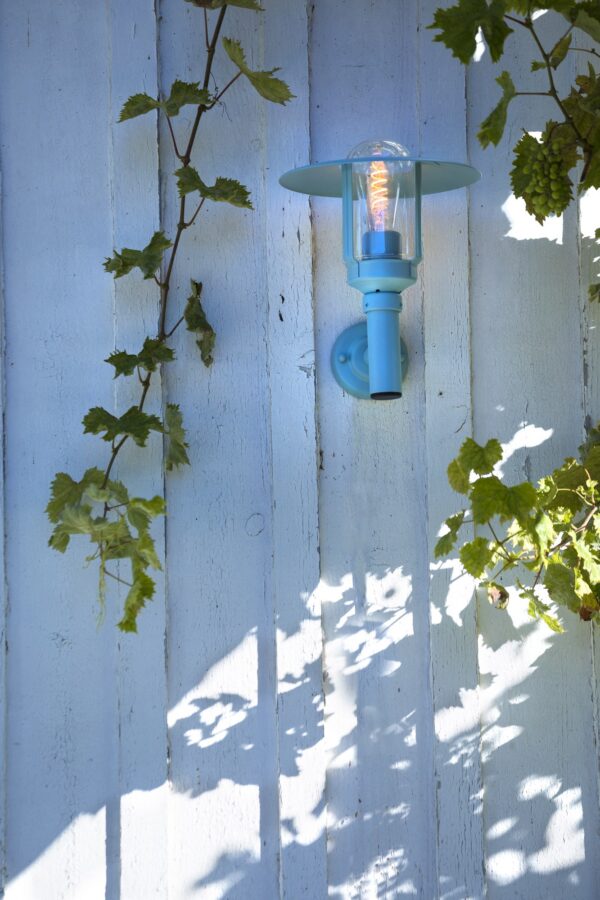 applique montante Newpark en aluminium bleu fixée sur un mur de planches peintes sous une vigne