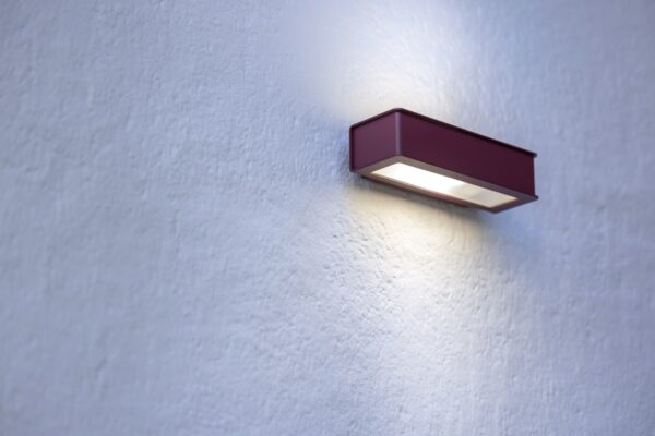 applique Plémo rouge vin allumée sur un mur enduit avec éclairage haut et bas