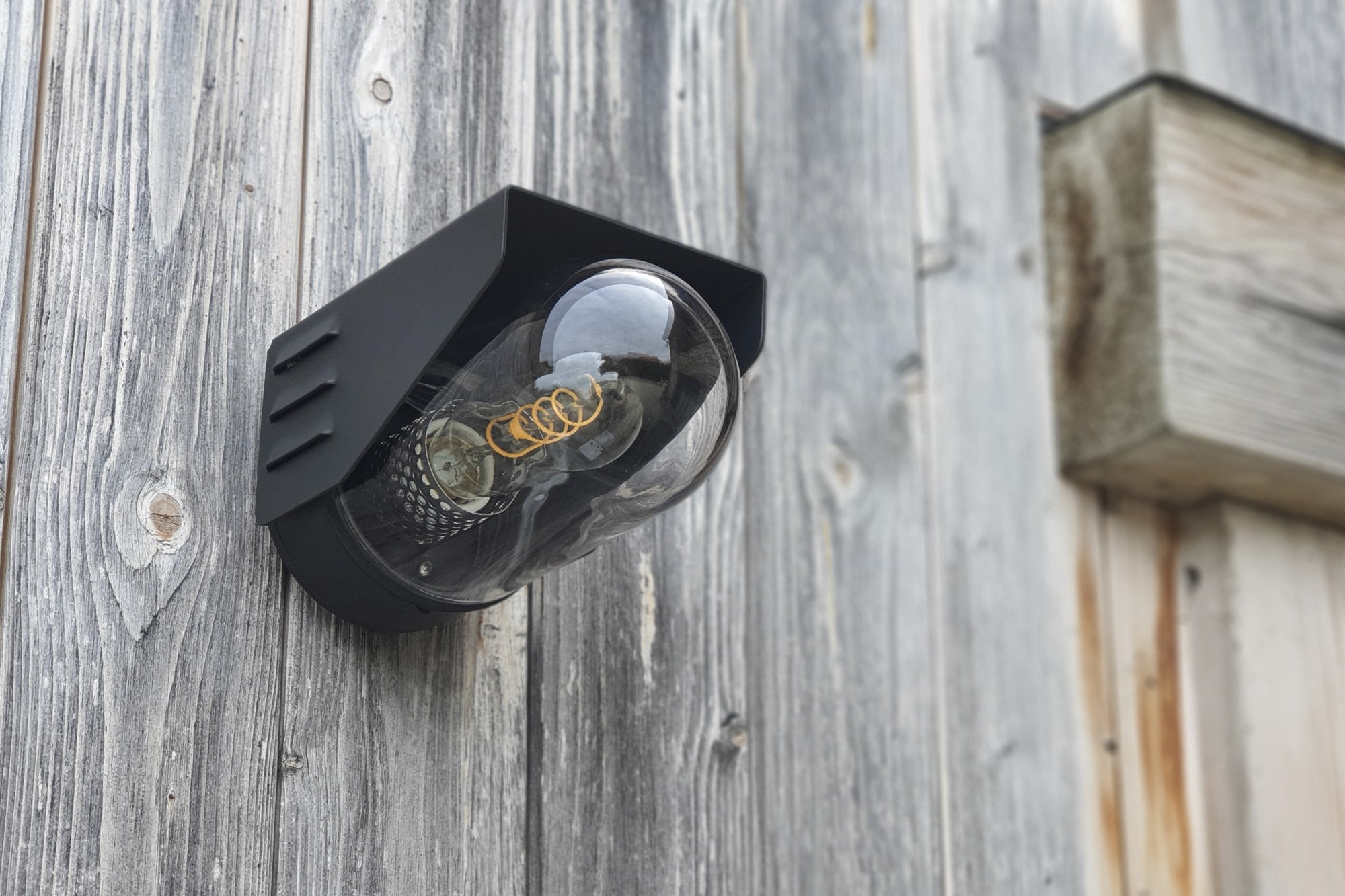 Applique RP195 en aluminium IP65, 2 tailles, Roger Pradier applique RP195 noir velours avec ampoule à filament sur un mur de planches grisées