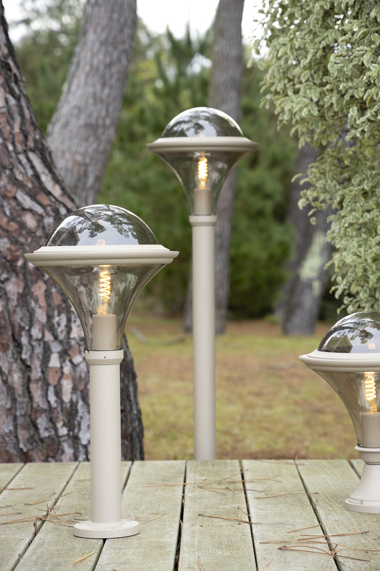Borne Dallas 1267 mm avec ou sans prise par Roger Pradier borne Dallas 1267 mm bornes de hauteurs différentes teinte grès avec vasque fumée sur une terrasse en bois dans un jardin
