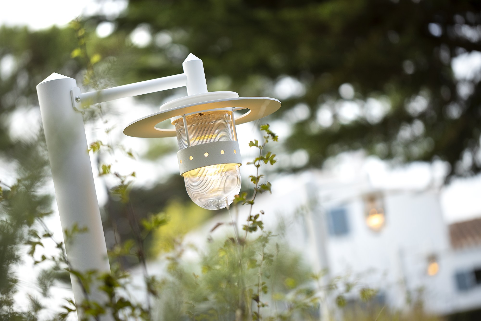 Borne extérieure Kent en aluminium par Roger Pradier borne extérieure Kent en blanc pur, gros plan sur la lanterne allumée dans un jardin