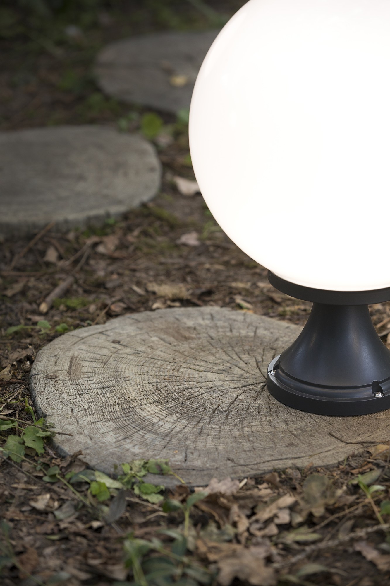 Borne Moon globe 300 mm en aluminium par Roger Pradier borne Moon globe 300 mm N° 6 en aluminium noir avec globe opale posée sur une souche de bois