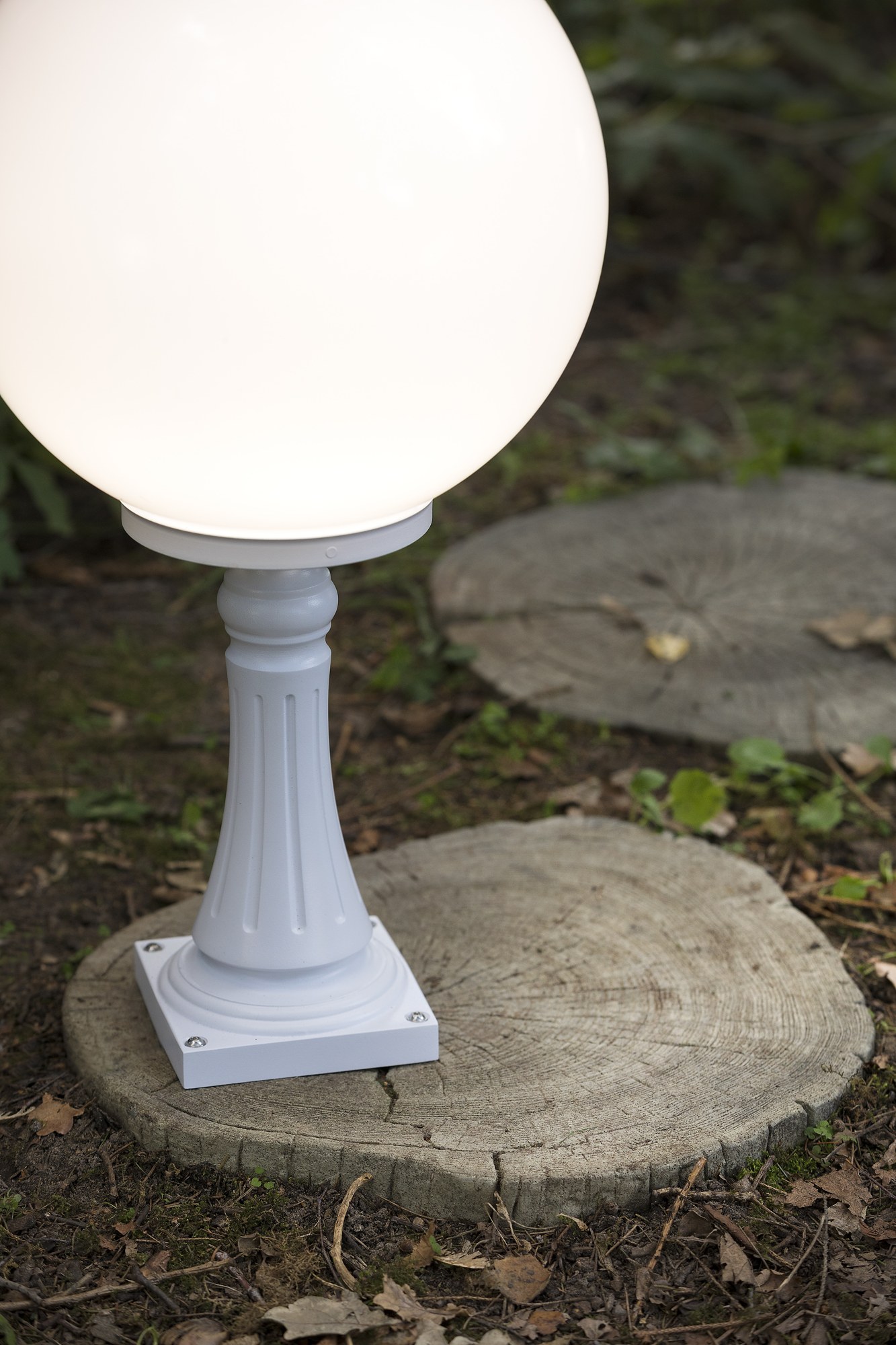 Borne Moon globe 300 mm en aluminium par Roger Pradier borne Moon globe 300 mm N° 7 en aluminium blanc avec globe opale posée sur une souche dans un sous-bois