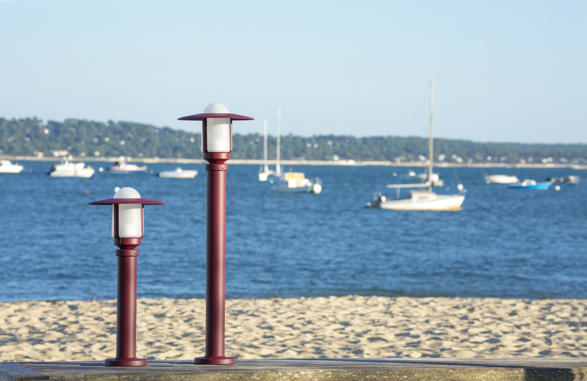 Borne Newpark par Roger Pradier en aluminium, 3 hauteurs borne Newpark en aluminium rouge vin sur une plage face à la mer et aux voiliers