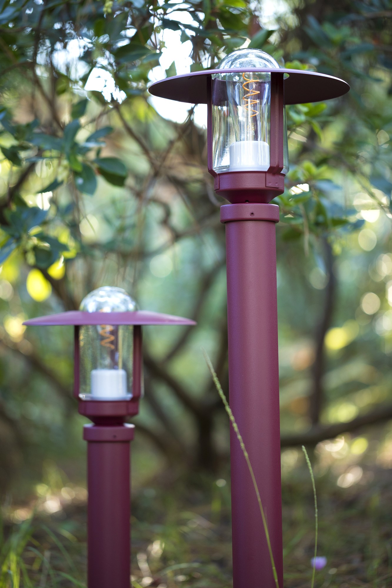 Borne Newpark par Roger Pradier en aluminium, 3 hauteurs deux bornes Newpark de hauteurs différentes en rouge vin dans un massif de feuillage