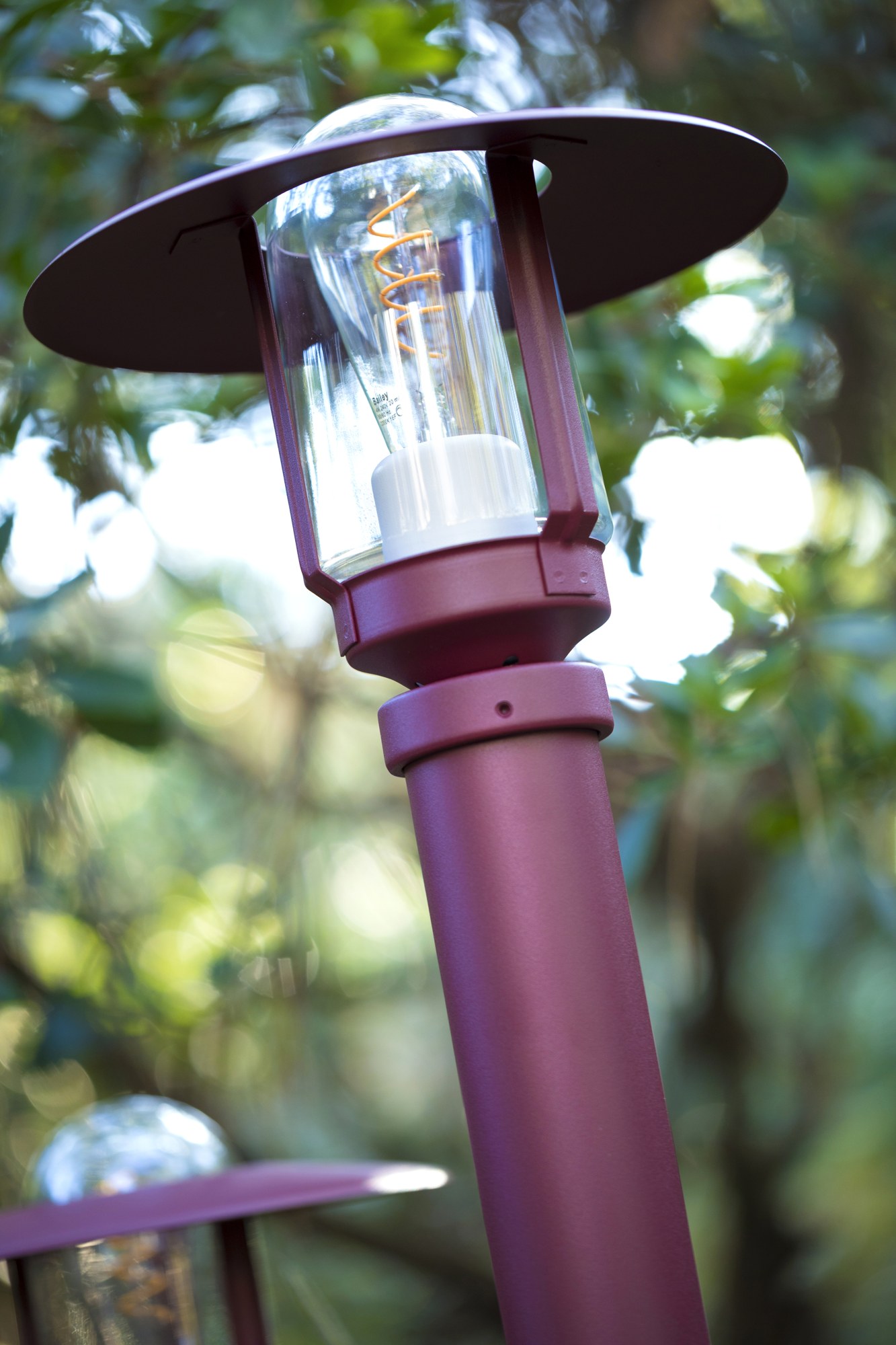 Borne Newpark par Roger Pradier en aluminium, 3 hauteurs borne Newpark rouge vin, gros plan sur la lanterne, le chapeau et l ampoule à filament