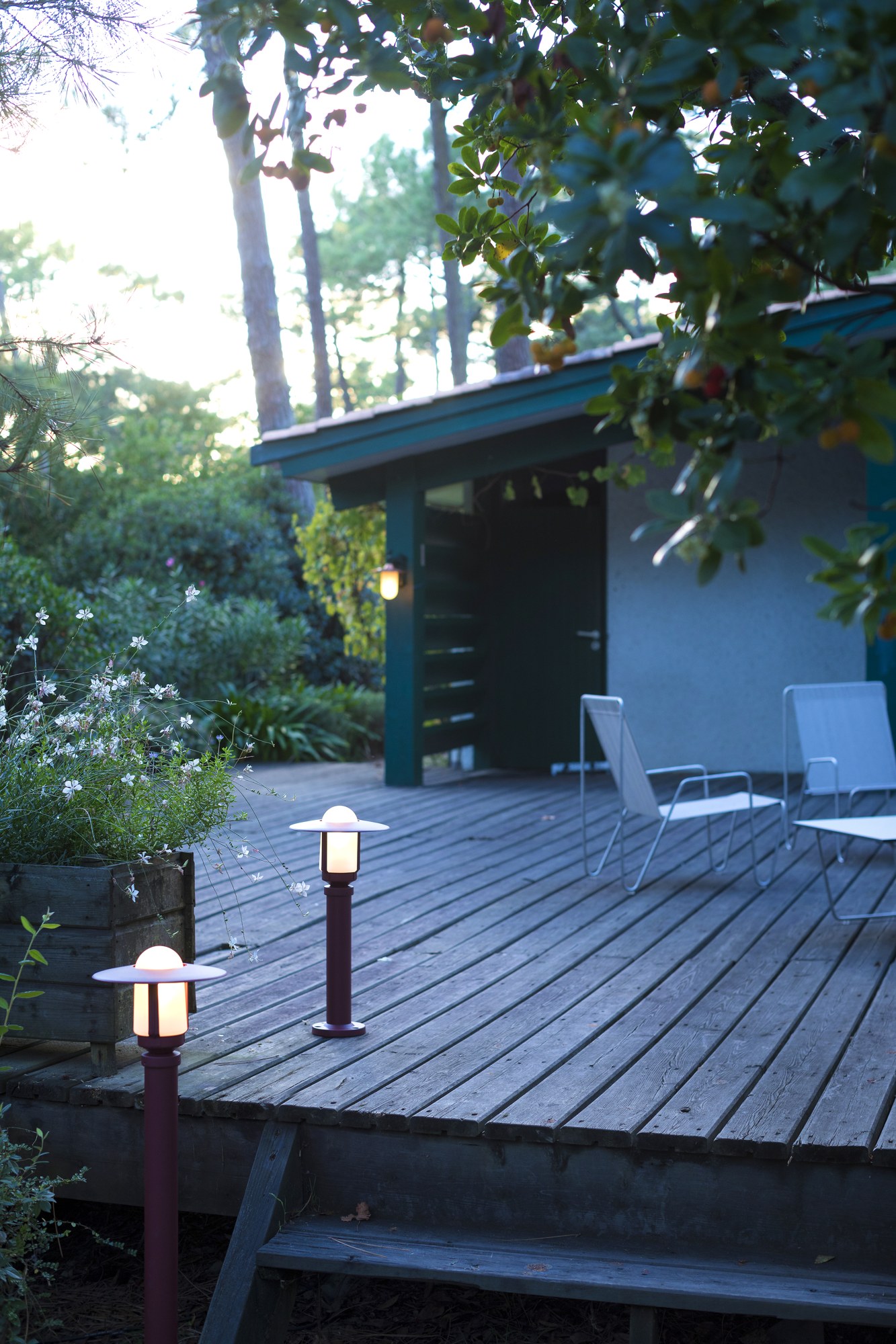 Borne Newpark par Roger Pradier en aluminium, 3 hauteurs borne Newpark rouge vin éclairant une terrasse en bois devant une cabane de jardin