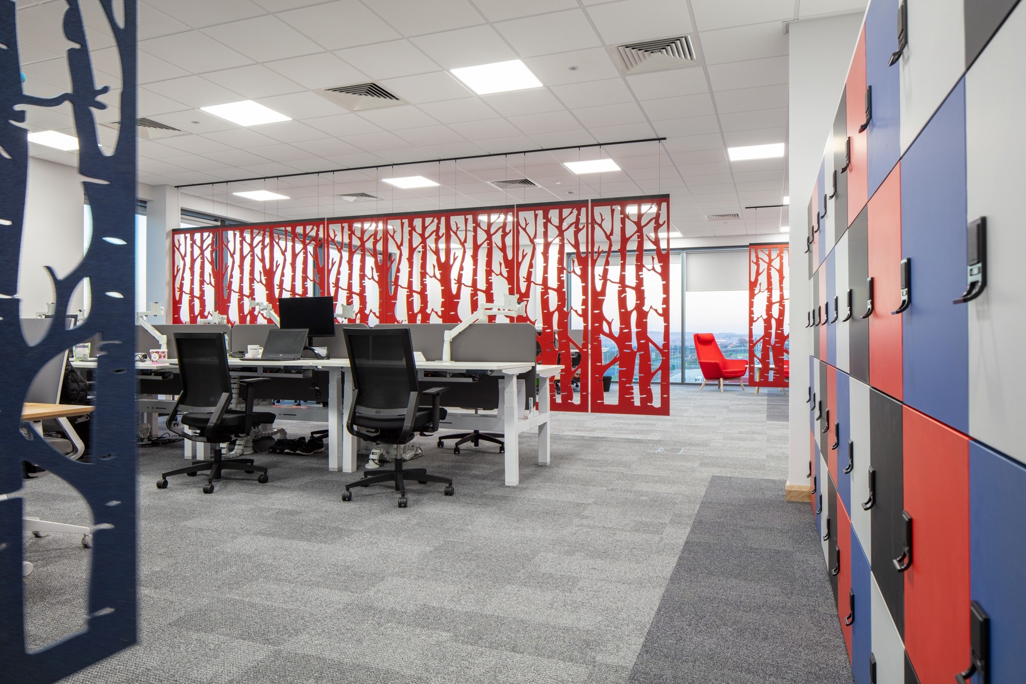 Cloison suspendue BuzziFalls par BuzziSpace, feutre à motifs découpés cloison suspendue BuzziFalls en feutre rouge au motif Birch entre des postes de travail
