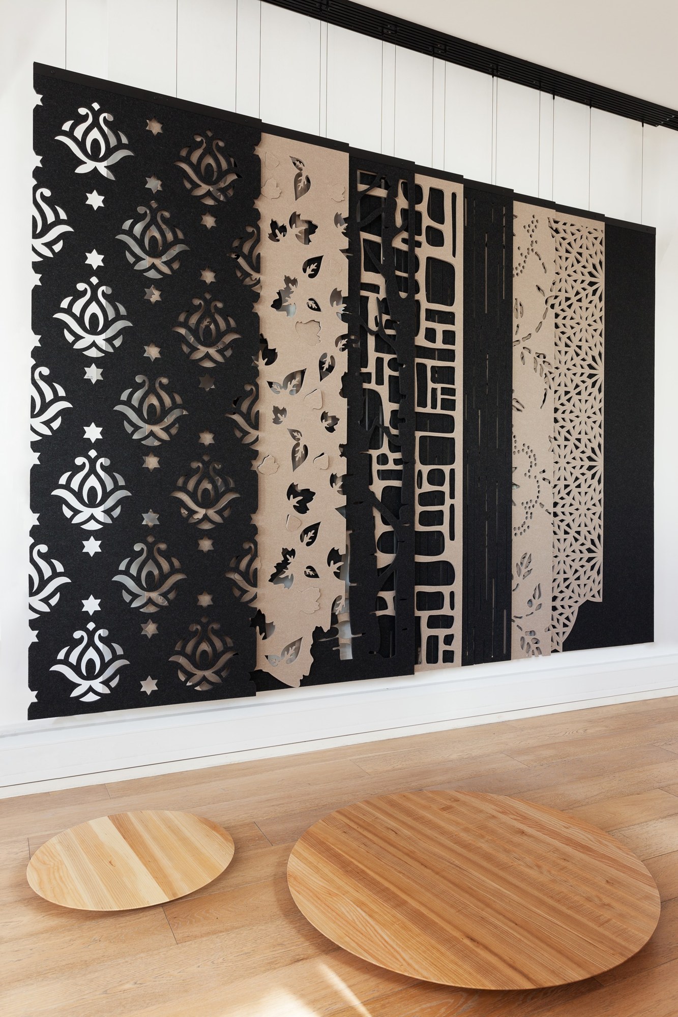 Cloison suspendue BuzziFalls par BuzziSpace, feutre à motifs découpés cloison suspendue BuzziFalls, panneaux de feutre noir et beige à motifs variés fixés sur un rail