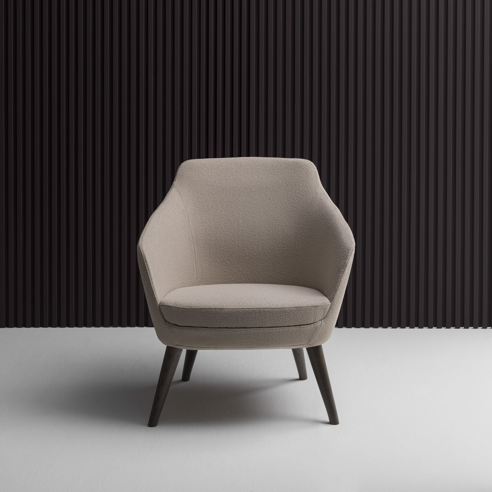 Fauteuil d'accueil Setar par Bralco, canapé 2 places, luge ou pieds bois fauteuil Setar Bralco en tissu beige devant un mur de lames noires, vue de face