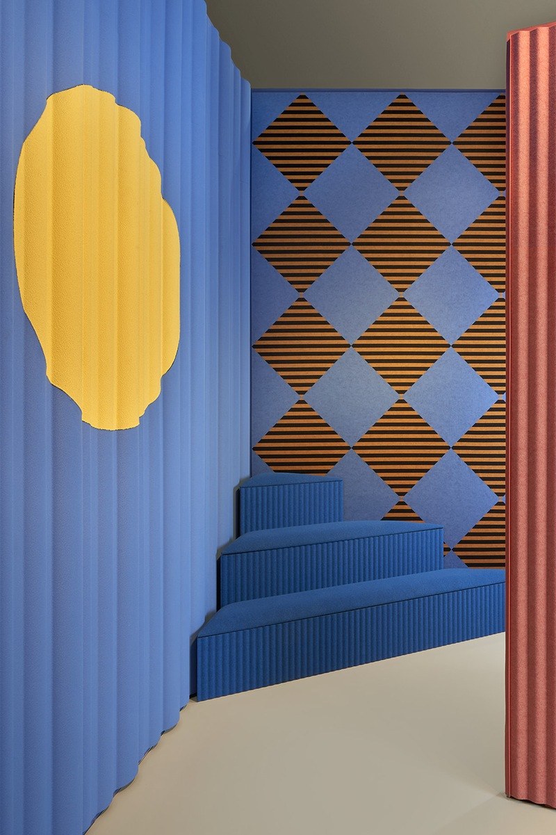 Feutre acoustique imprimé Arlecchino Felt par Slalom, mur à losanges feutre acoustique imprimé Slalom Arlecchino Felt sur un mur bleu pres de escalier
