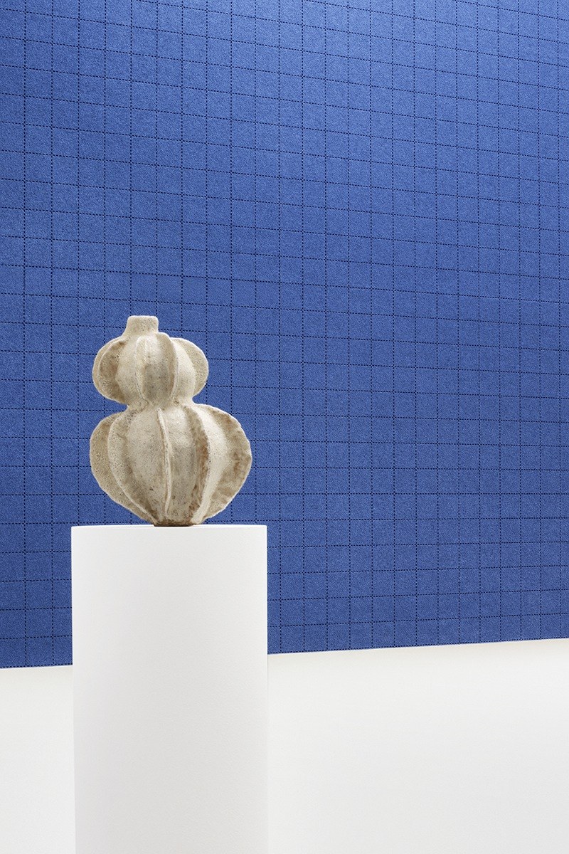 Feutre acoustique surpiqué CRAFTfelt par Slalom, quadrillage laser feutre acoustique surpiqué Slalom CRAFTfelt sur un mur bleu avec une sculpture