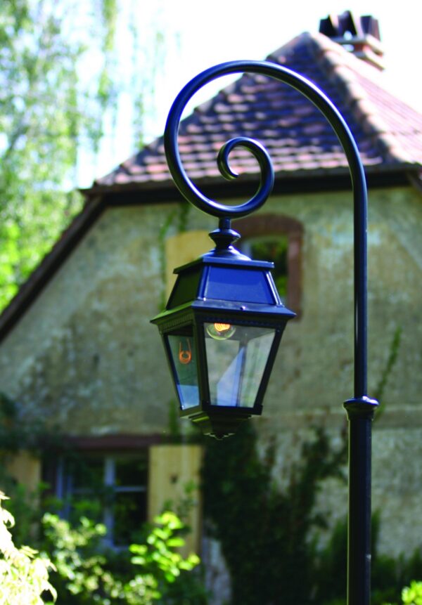 lampadaire Avenue 2 version crosse noire à volute dans un jardin devant une maison en pierre