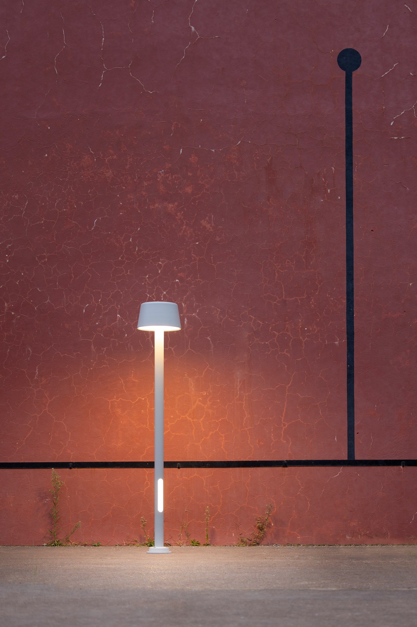 Lampadaire Bark par Roger Pradier, mât aluminium LED ou E27 lampadaire Bark gris soie allumé devant un mur rouge avec sa fente lumineuse basse