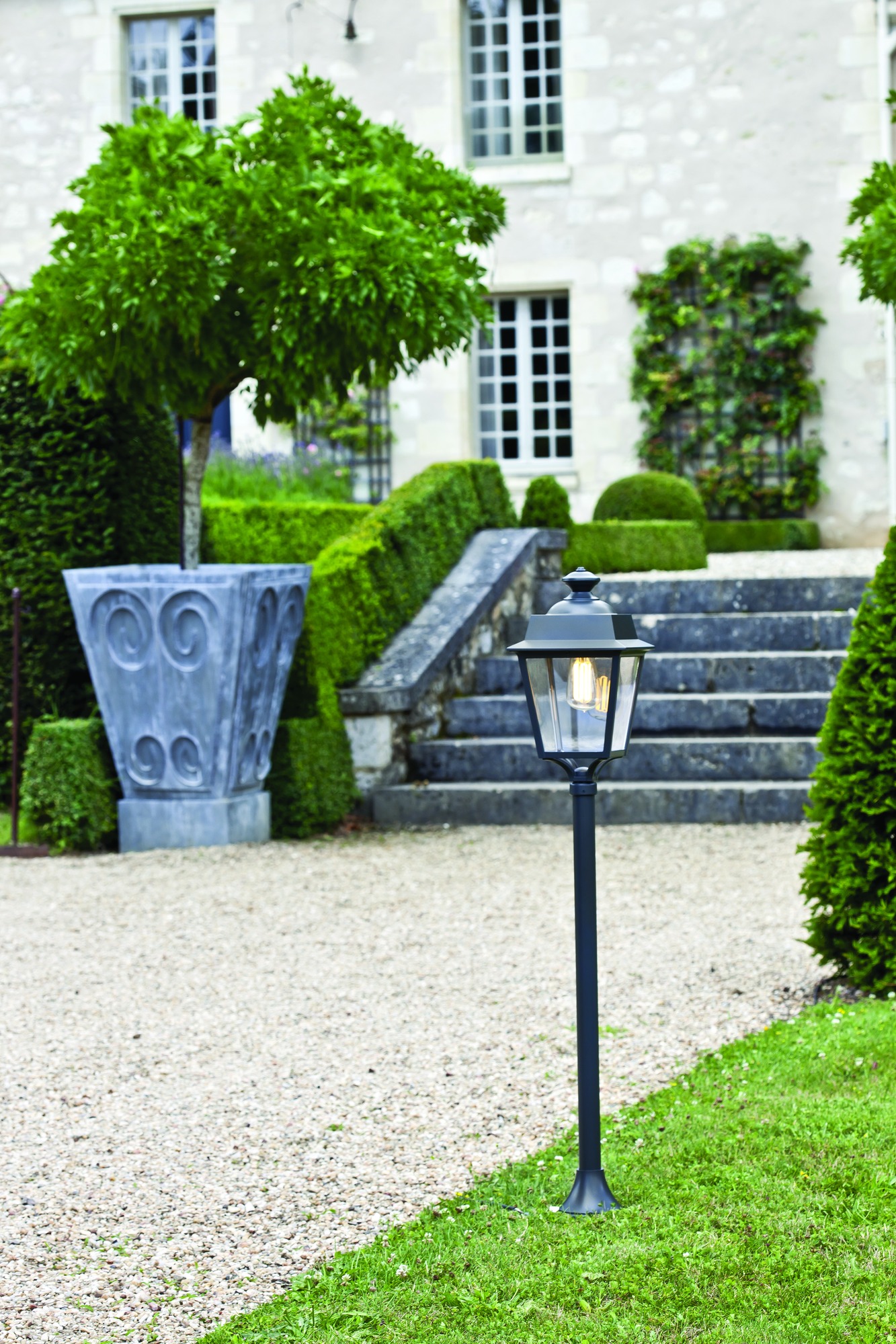 Lampadaire Place des Vosges Évolution en aluminium par Roger Pradier lampadaire Place des Vosges Évolution colonne lisse basse allumé dans une allée de gravier devant une demeure en pierre