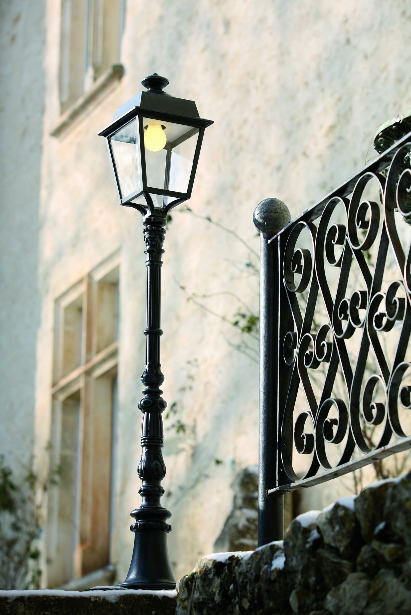 Lampadaire Place des Vosges Évolution en aluminium par Roger Pradier lampadaire Place des Vosges Évolution colonne ornée devant un mur crépi et une grille en fer forgé