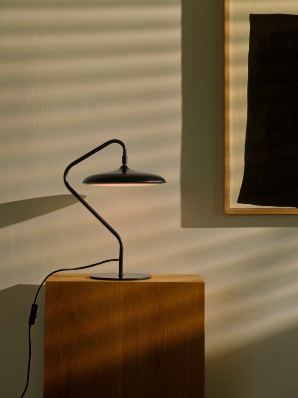 lampe à poser Artist noire posée sur un socle en bois, lumière chaude