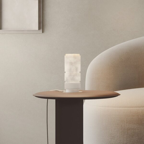 lampe à poser Bowie allumée sur une petite table ronde près du canapé arrondi beige