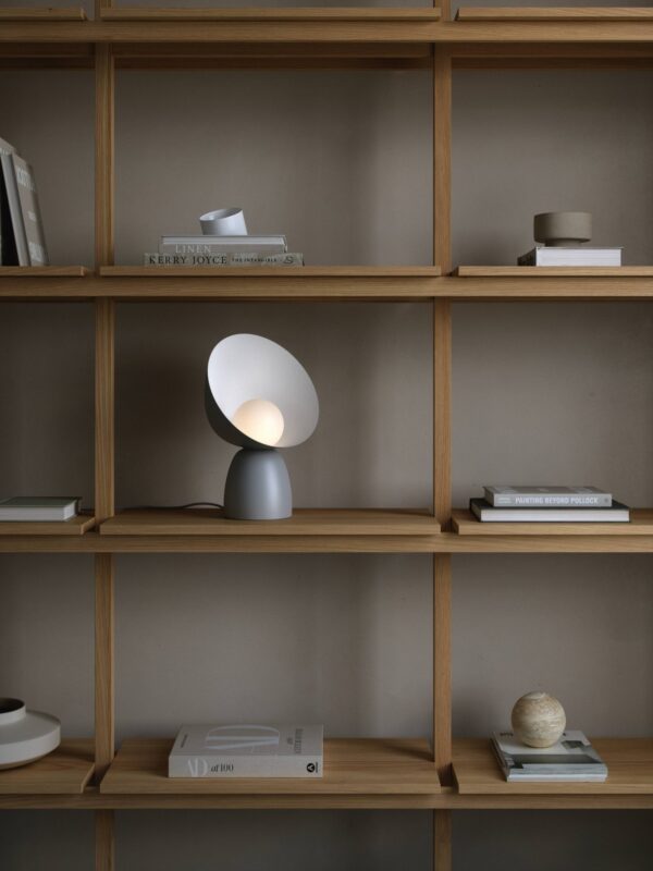 lampe à poser Hello grise posée dans une bibliothèque en bois