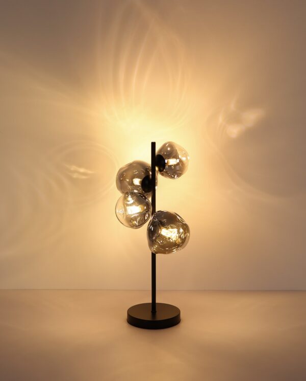 lampe à poser verre fumé 4 lumières allumée, reflets de lumière chaude sur le mur