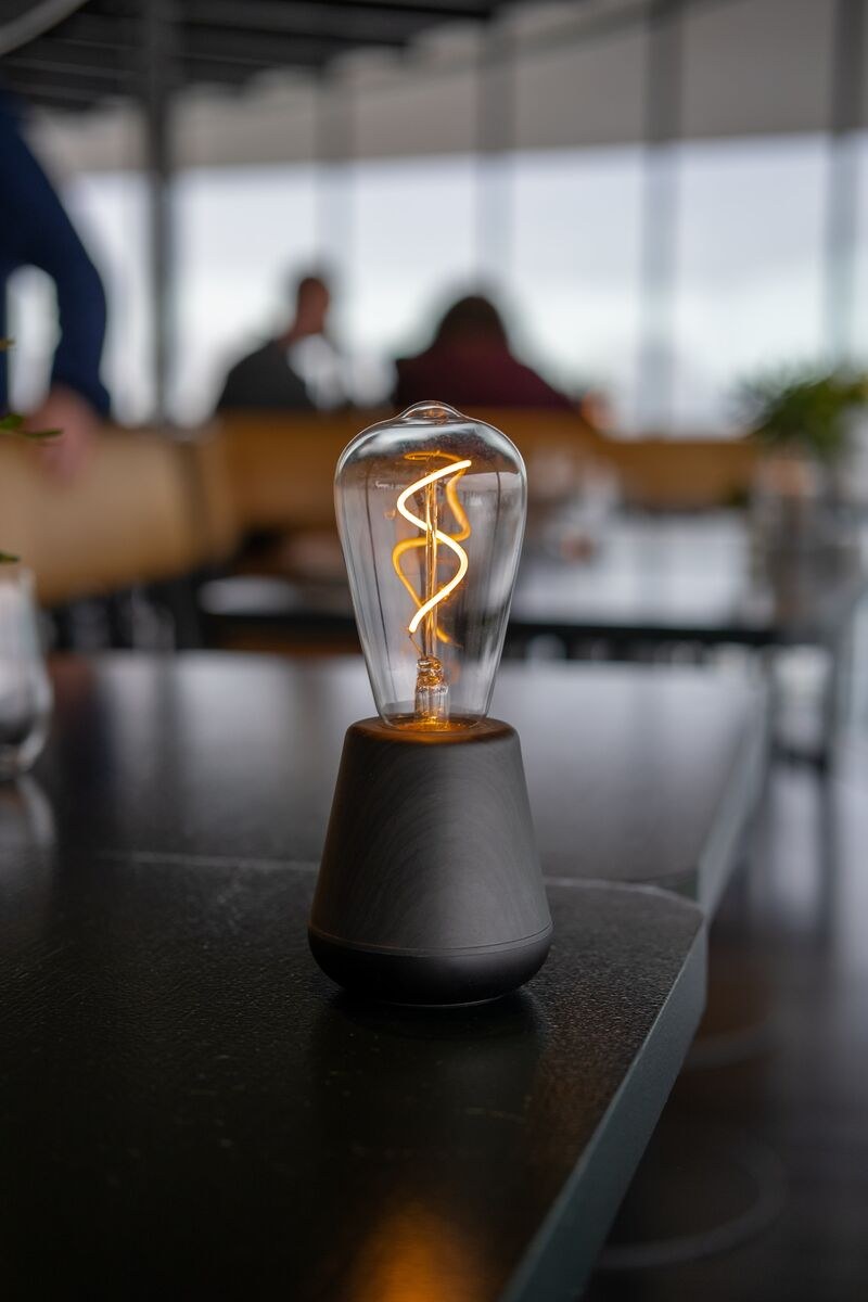Lampe rechargeable One par Humble, ampoule à filament visible lampe rechargeable One Humble, finition Black Wood sur une table de restaurant