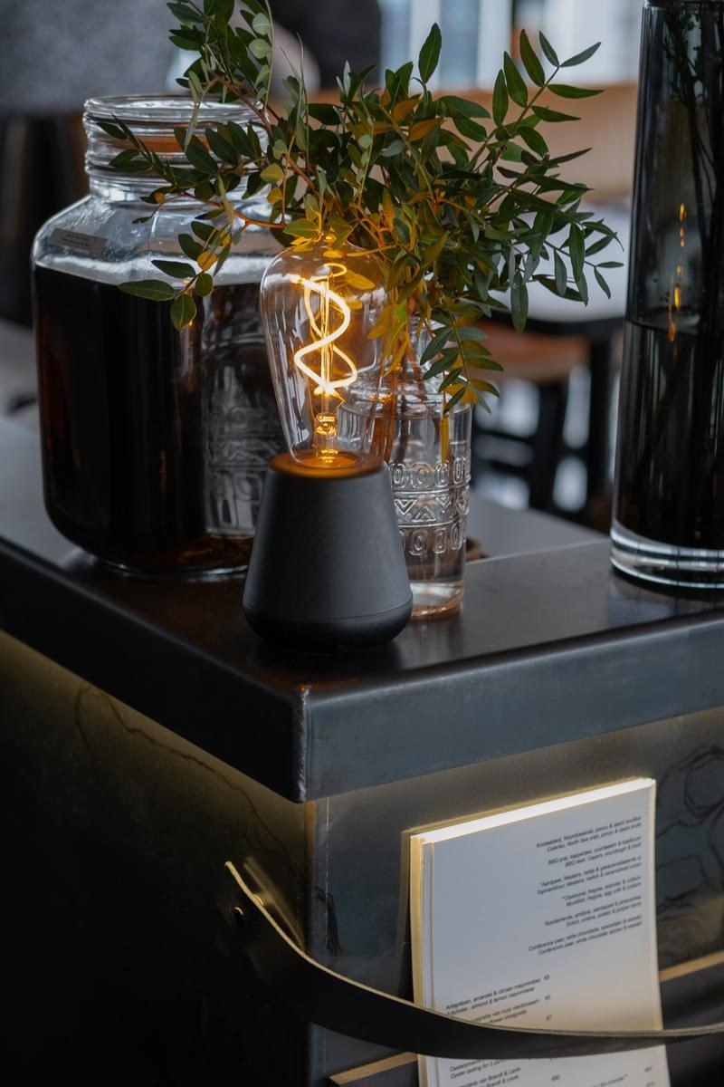 Lampe rechargeable One par Humble, ampoule à filament visible lampe rechargeable One Humble, finition Black Wood allumée au milieu d'une table