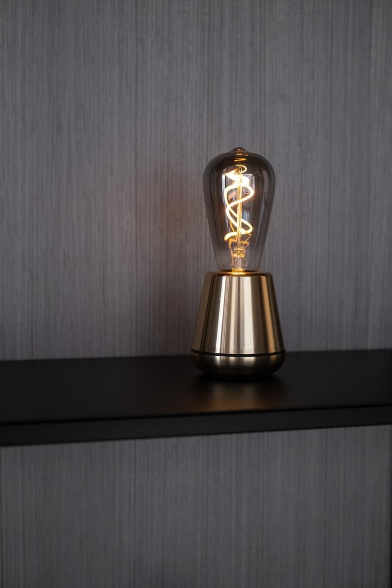 Lampe rechargeable One par Humble, ampoule à filament visible lampe rechargeable One Humble, finition Gold allumée sur une table en bois