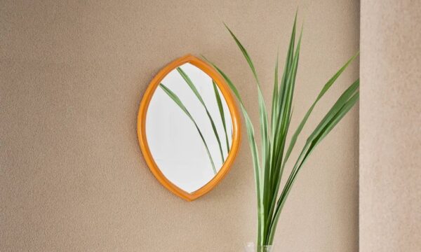 miroir Jamie Urban Nature Culture accroché sur un mur près d'un grand bouquet de feuilles