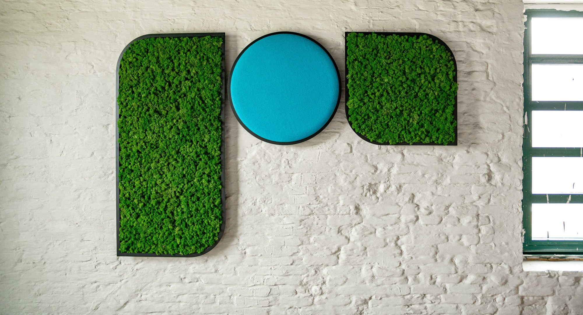 Panneau acoustique BuzziMood par BuzziSpace, mousse végétale ou tissu panneau acoustique BuzziMood BuzziSpace, panneaux de mousse verte et rond en tissu turquoise sur un mur de brique blanche