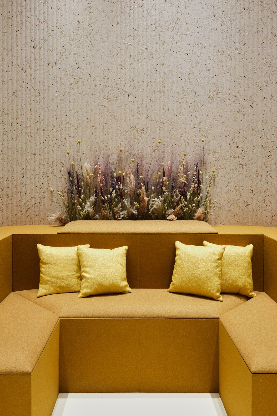 Panneau acoustique herbes naturelles Grass par Slalom, lin et foin panneau acoustique herbes naturelles Slalom Grass derriere une banquette moutarde et des fleurs seches