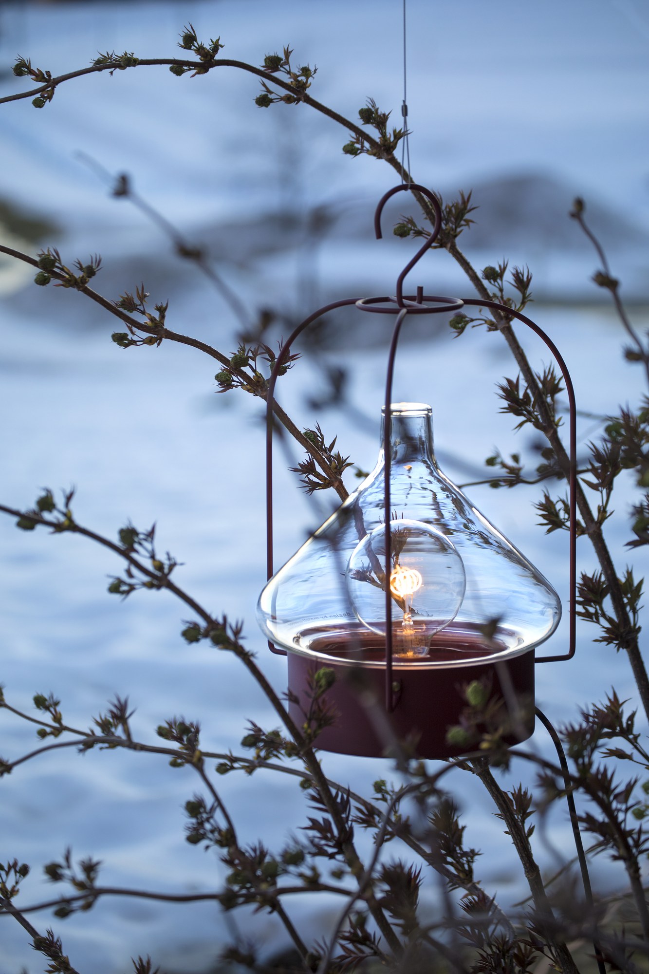 Suspension nomade La Hutte par Roger Pradier, verre soufflé suspension nomade La Hutte teinte rouge vin suspendue dans des branches devant la neige