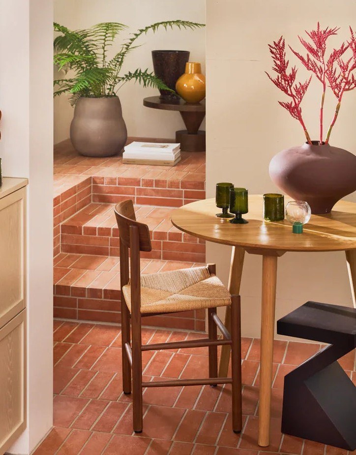 Table d'appoint Gama par Urban Nature Culture, manguier noyer foncé table d'appoint bois Gama Urban Nature Culture, au pied d'une table ronde dans un coin repas aux sols en briques
