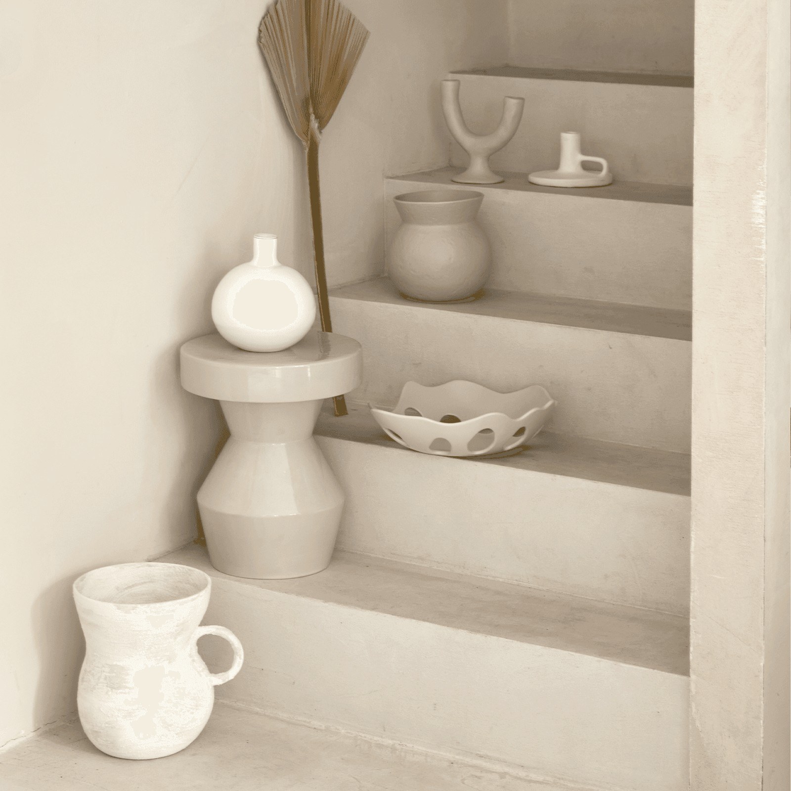 Table d'appoint Sculpturale par Urban Nature Culture, céramique table d'appoint céramique Sculpturale Urban Nature Culture, coloris peyote dans un escalier en enduit clair avec des vases blancs