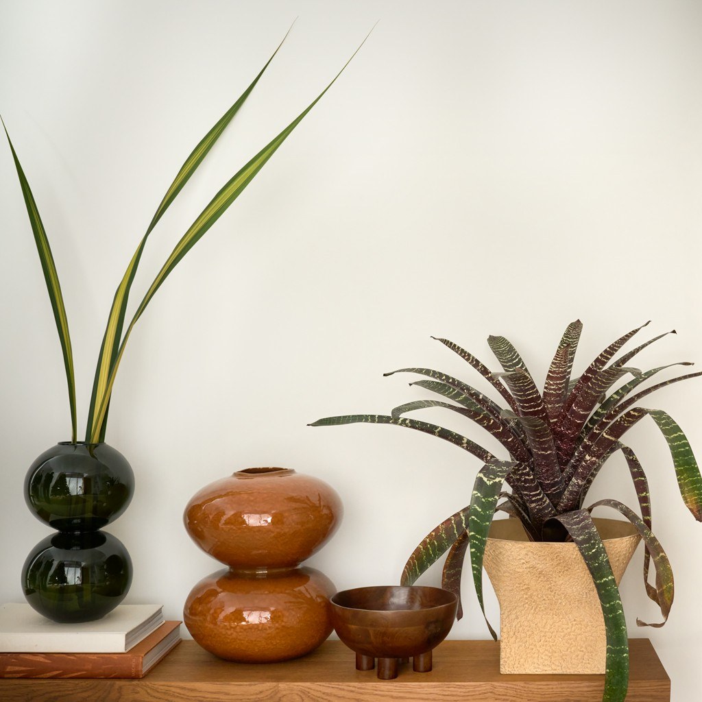 Vase Fossile par Urban Nature Culture, céramique, 2 coloris vase céramique Fossile Urban Nature Culture, coloris orange cuivré, posé sur une console en bois près d'un vase en verre vert
