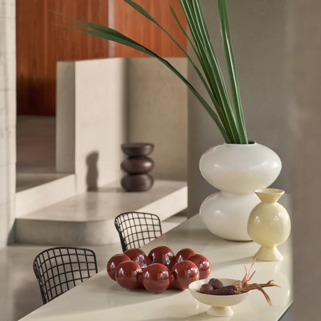 Vase Fossile par Urban Nature Culture, céramique, 2 coloris vase céramique Fossile Urban Nature Culture, coloris blanc cassé, sur une table claire avec de longues feuilles vertes